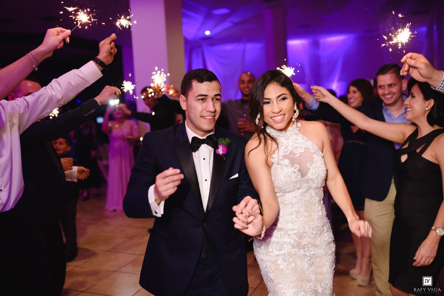 Bride and groom walk through sparkler tunnel at wedding reception, smiling joyfully in elegant attire.