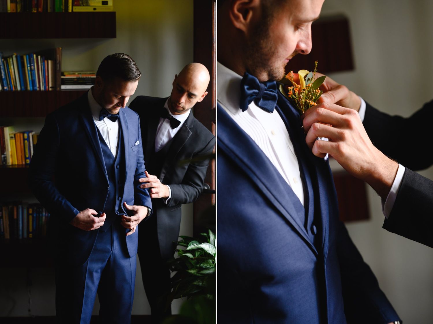 Groom in navy blue suit being helped by groomsmen while pinning orange boutonniere on lapel before wedding ceremony.