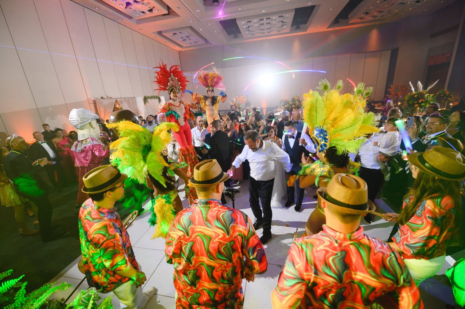 Colorful carnival performers in feathered costumes entertain guests at a vibrant indoor celebration event.