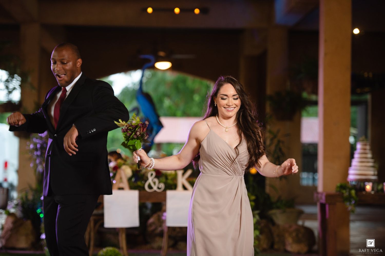 A man and woman in formal attire dance joyfully at an elegant wedding reception.