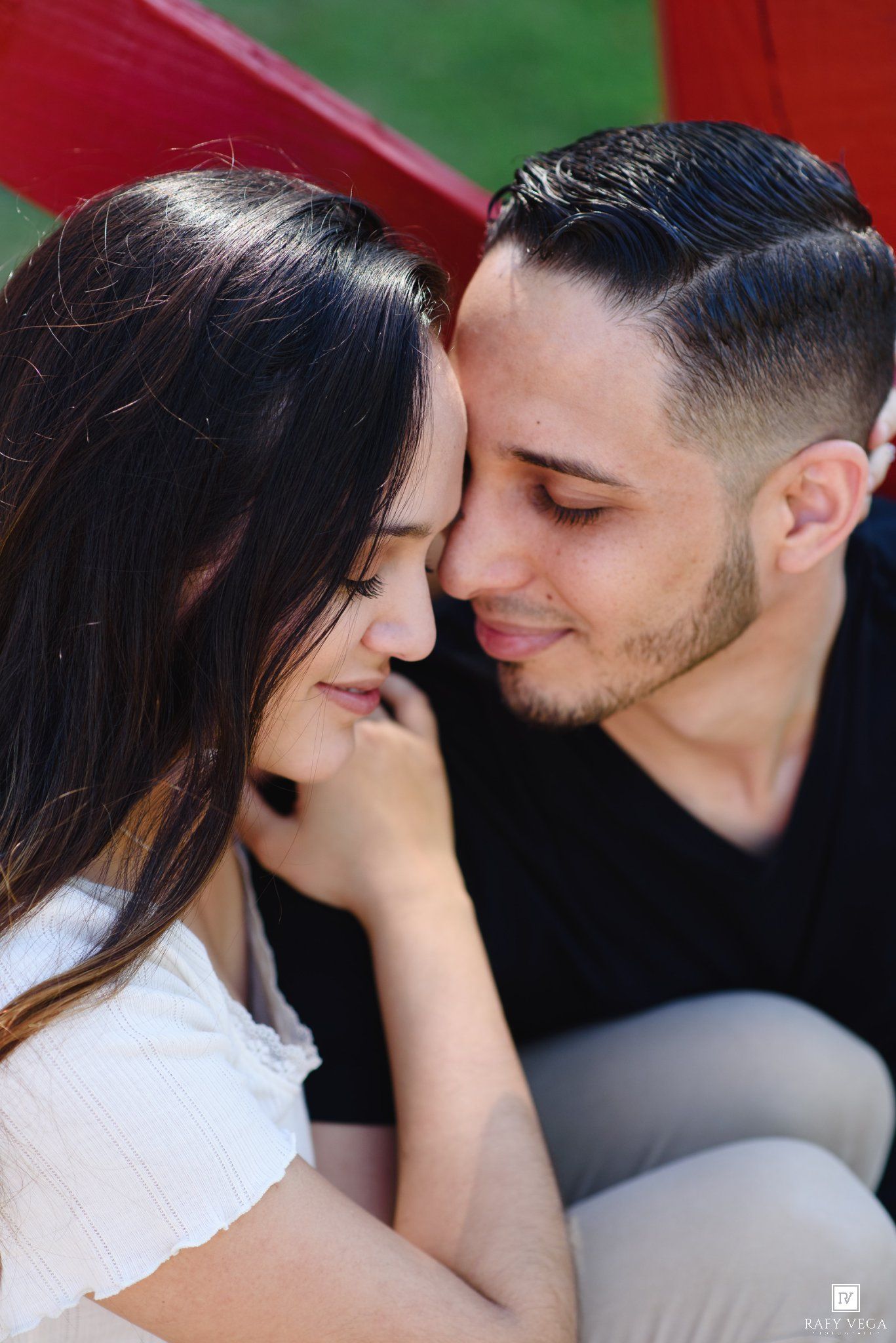 A romantic couple sharing an intimate moment, the man tenderly nuzzling the smiling woman's cheek outdoors.