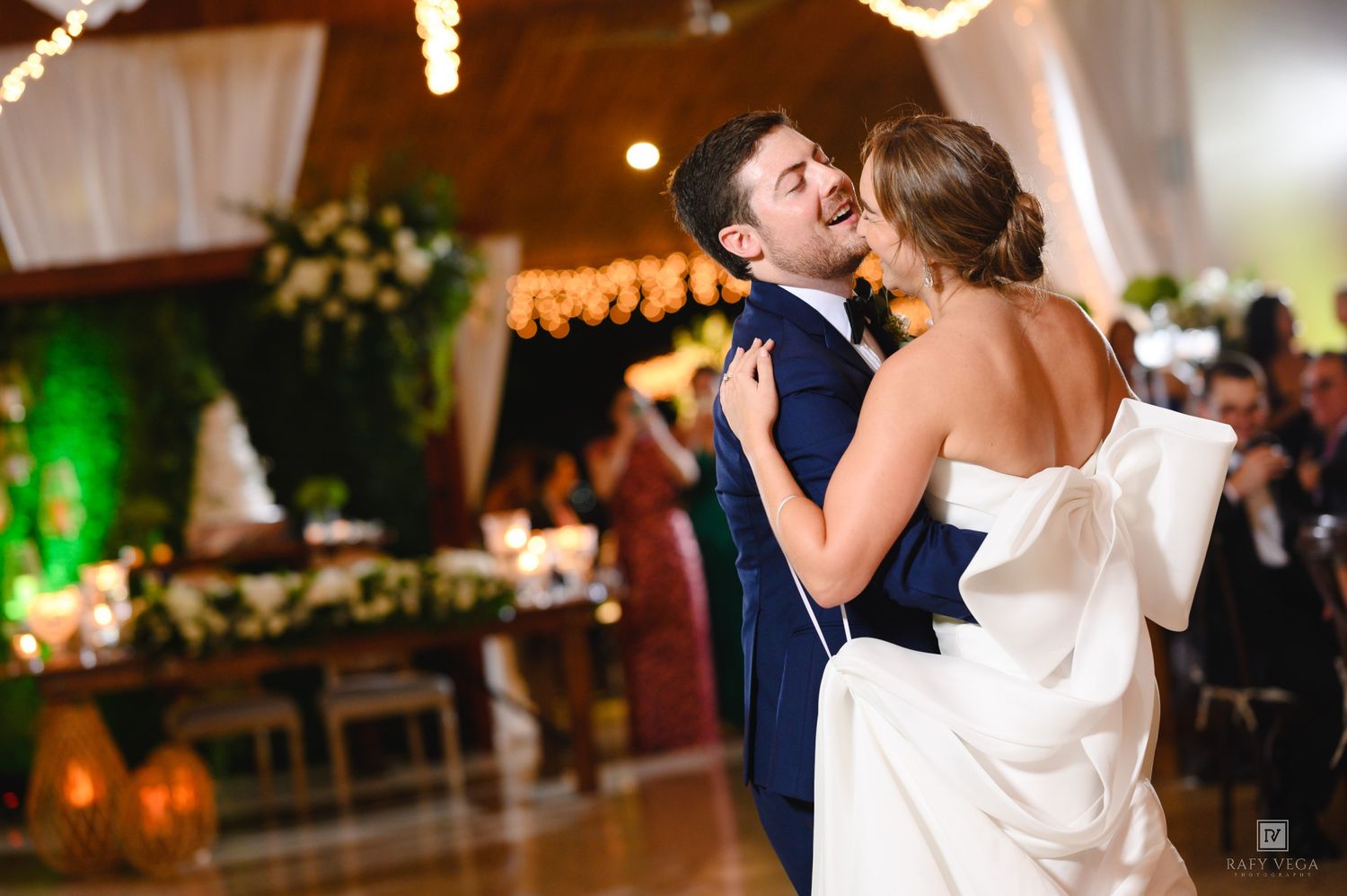 Bride and groom share their first dance at elegant wedding reception with warm string lights and floral decorations.