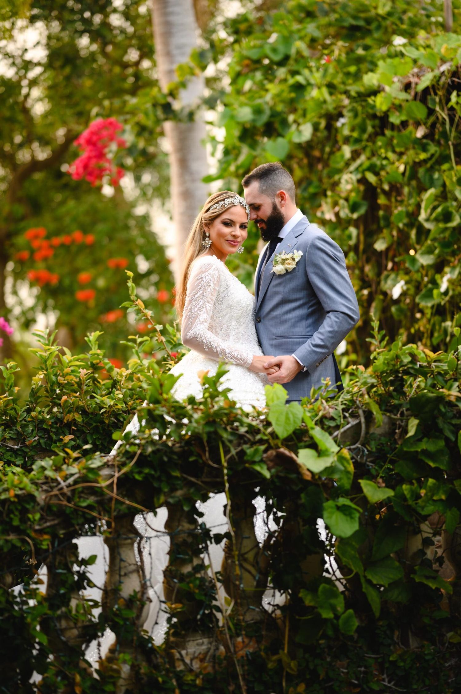 Bride and groom pose romantically among lush tropical greenery and colorful flowers on their wedding day.