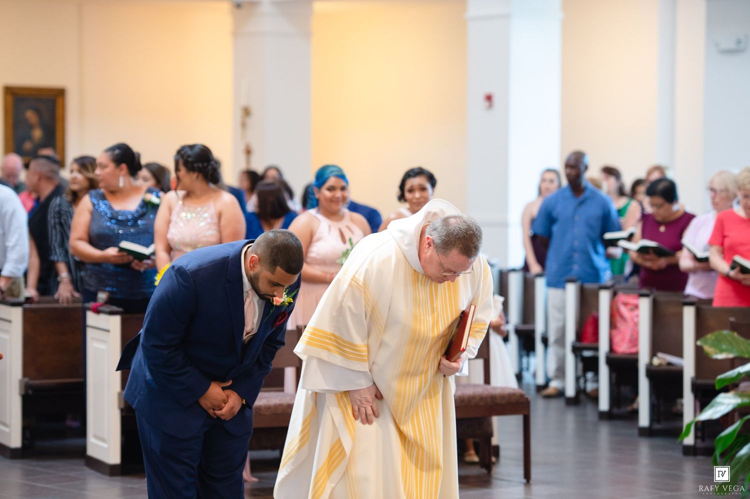 Groom and priest bowing at the altar during a wedding ceremony in a church filled with guests.