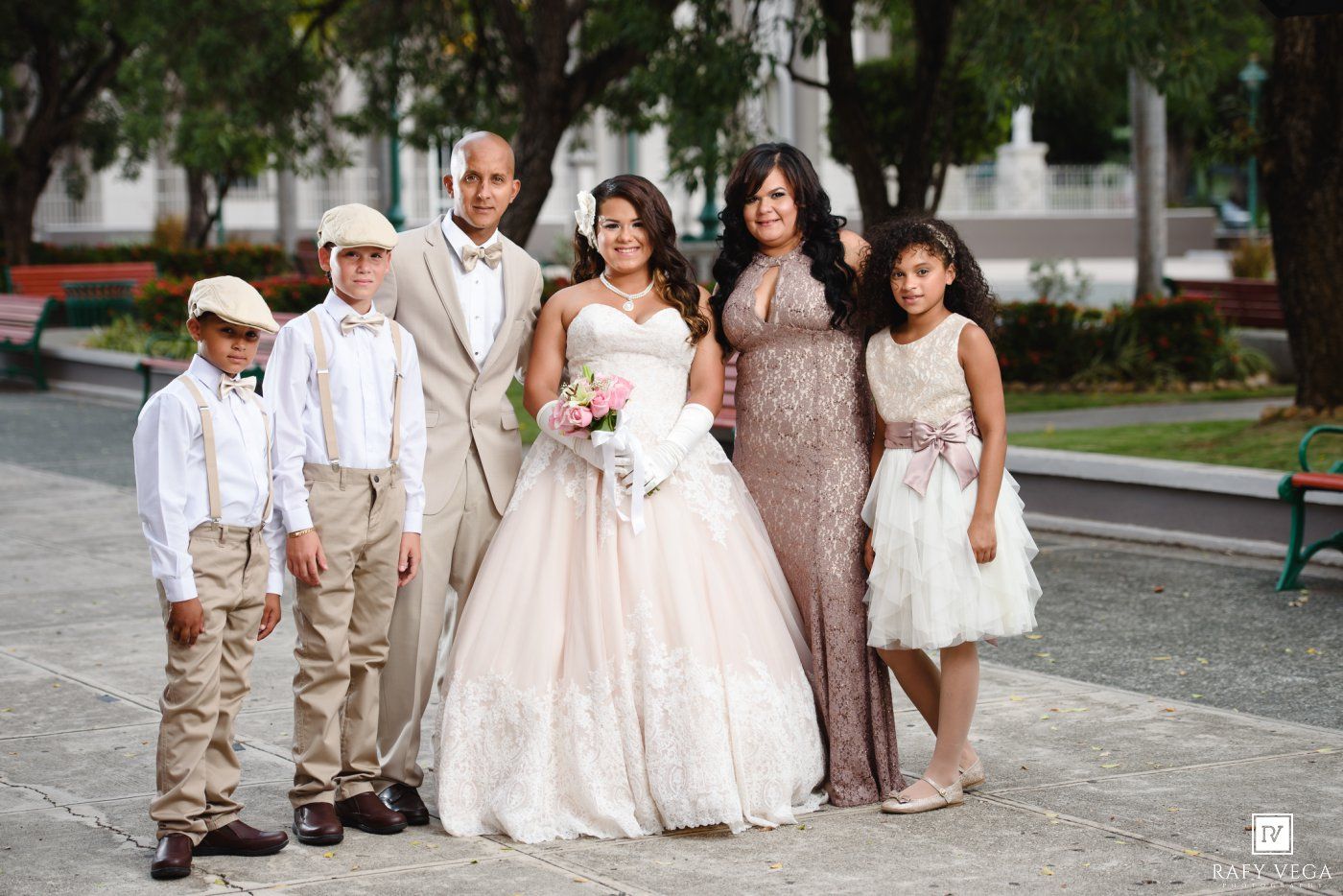 A bride in a white ball gown poses with family members in formal attire at an outdoor wedding celebration.