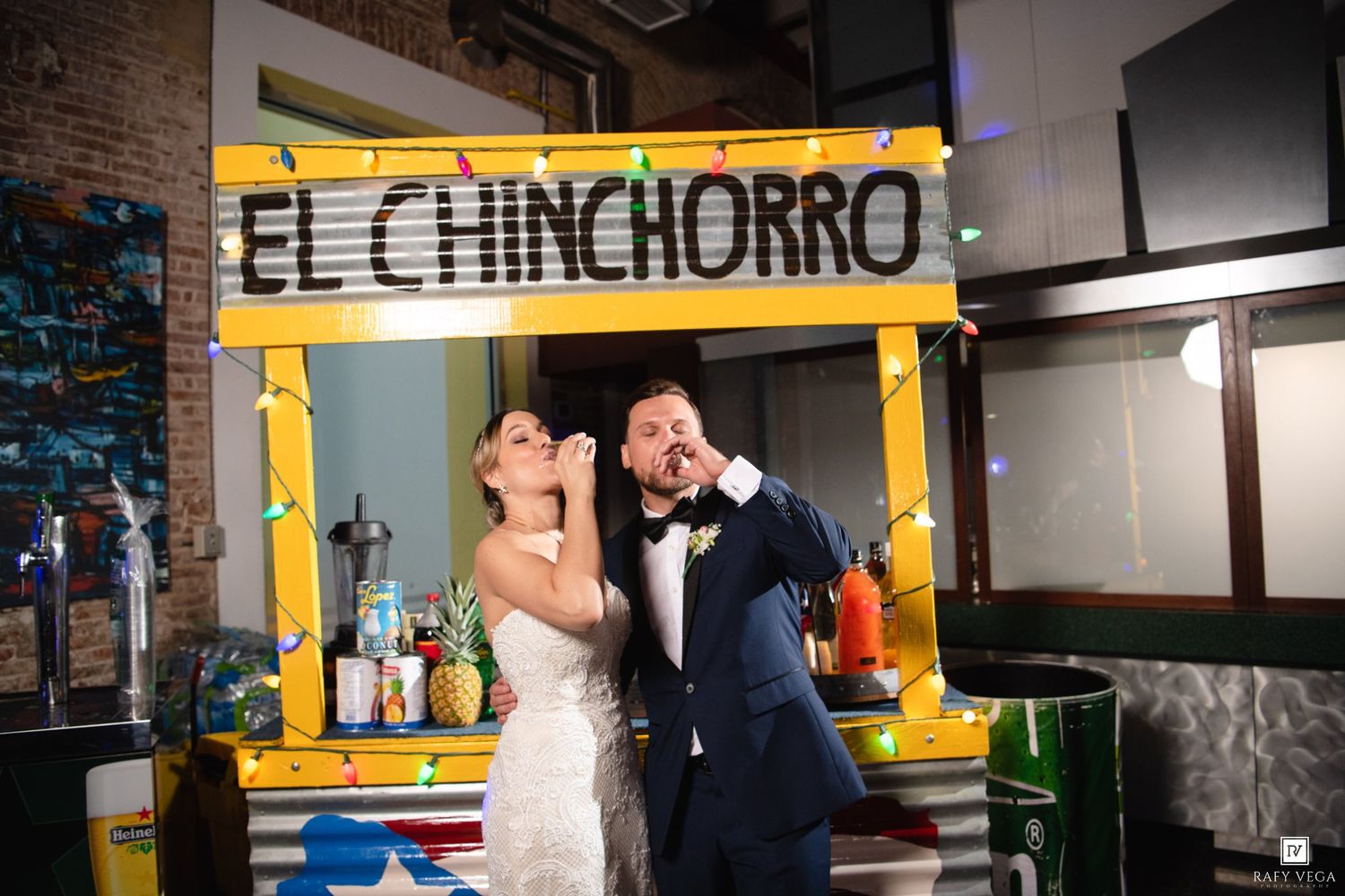 Bride and groom laughing and posing at El Chinchorro bar setup decorated with string lights at wedding reception.