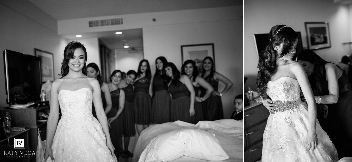 Black and white photo of a bride in a lace gown with bridesmaids in a hotel room.