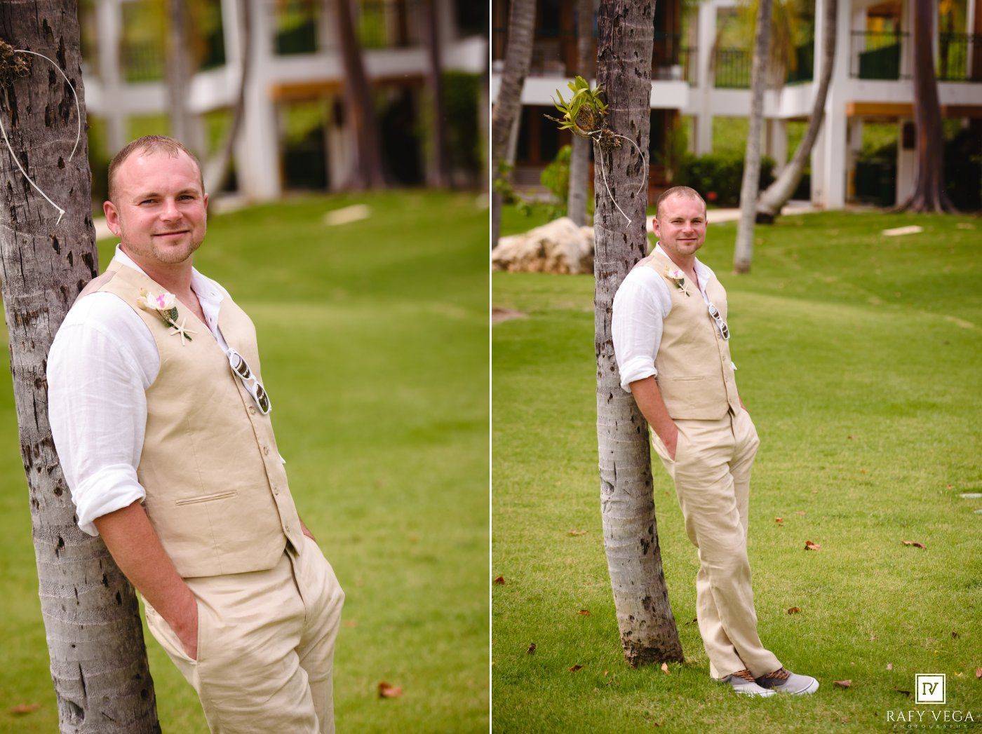 Groom in tan vest and khaki pants posing by a palm tree on a green lawn at an outdoor wedding.