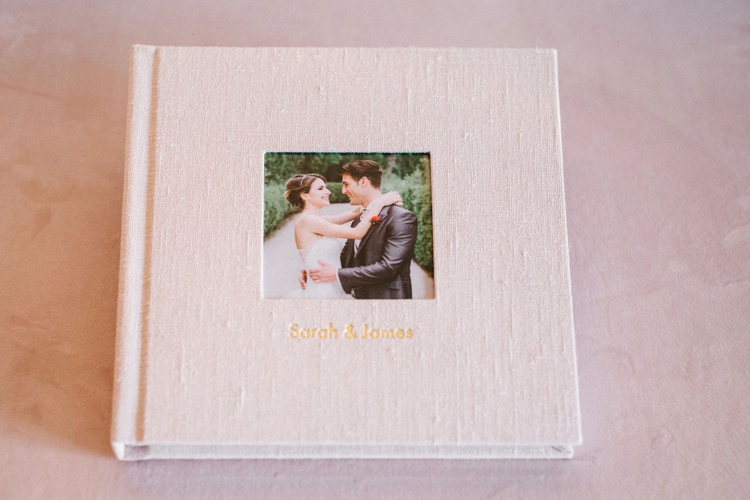 White linen wedding photo album with couple portrait window and gold personalized names on cover.