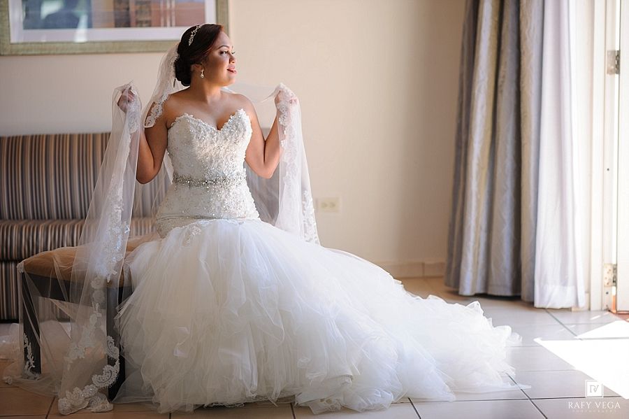 Bride in a strapless ball gown wedding dress holding her veil wide open in a sunlit room.