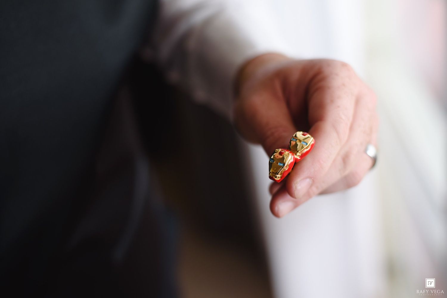 Close-up of a hand holding two ornate gold rings with intricate detailing at a wedding ceremony.