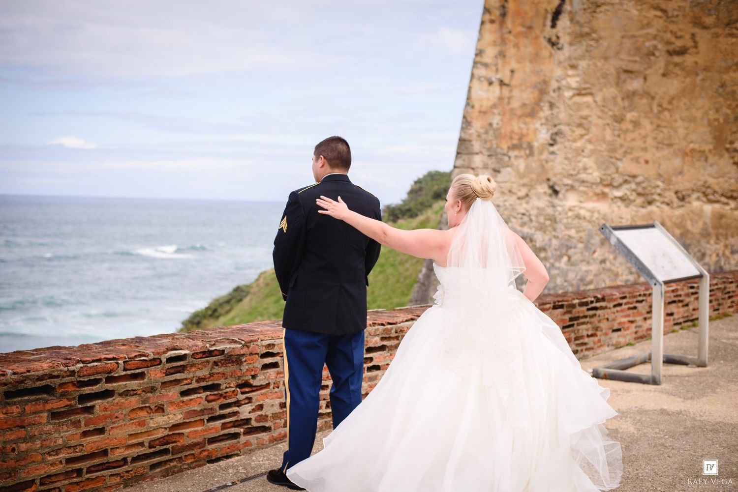 Bride and groom stand at a historic brick wall overlooking the ocean on their wedding day.