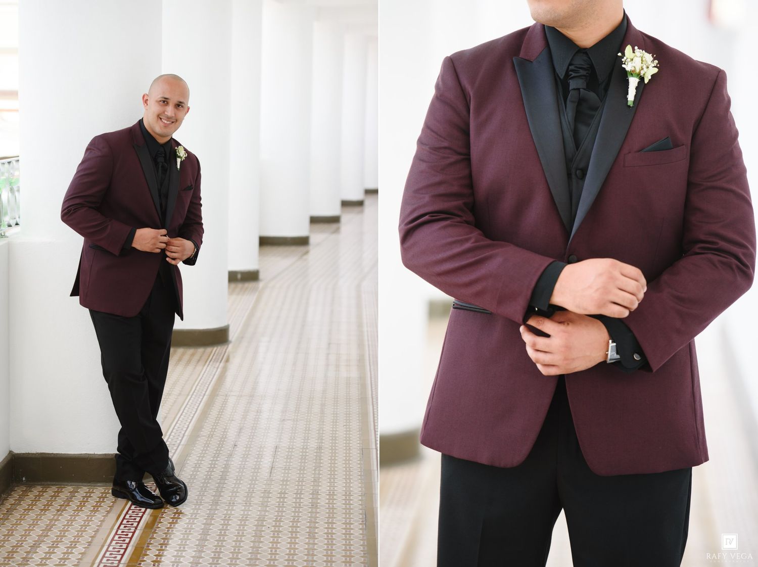 Groom in burgundy tuxedo jacket with black lapels, black shirt, and boutonniere poses in elegant venue hallway.