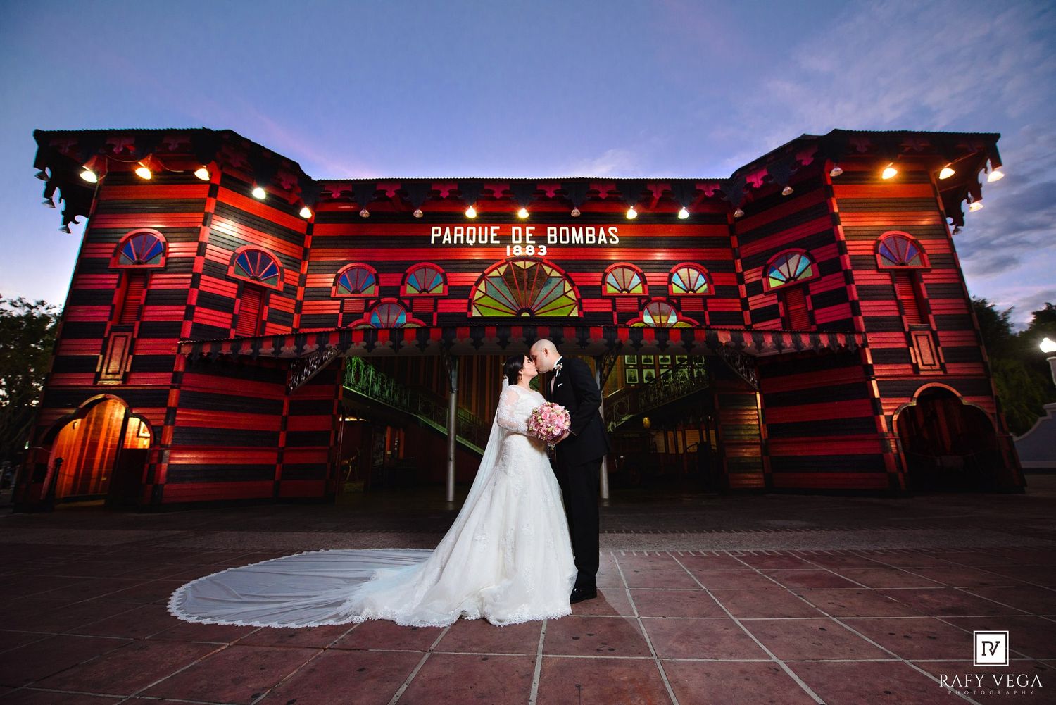 Wedding couple embracing before the colorful red Parque de Bombas landmark in Ponce, Puerto Rico at twilight.