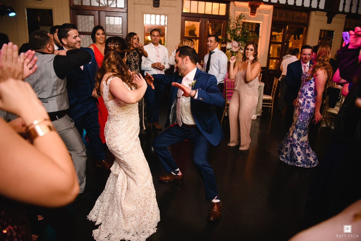 Bride and groom dancing joyfully with guests at elegant wedding reception venue.