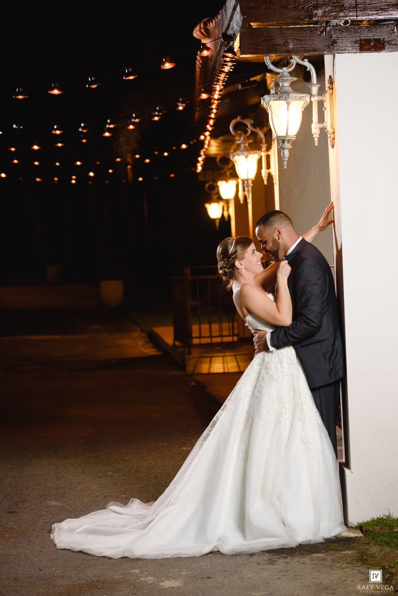 Bride and groom share a romantic kiss under glowing string lights and lanterns at night during their wedding.
