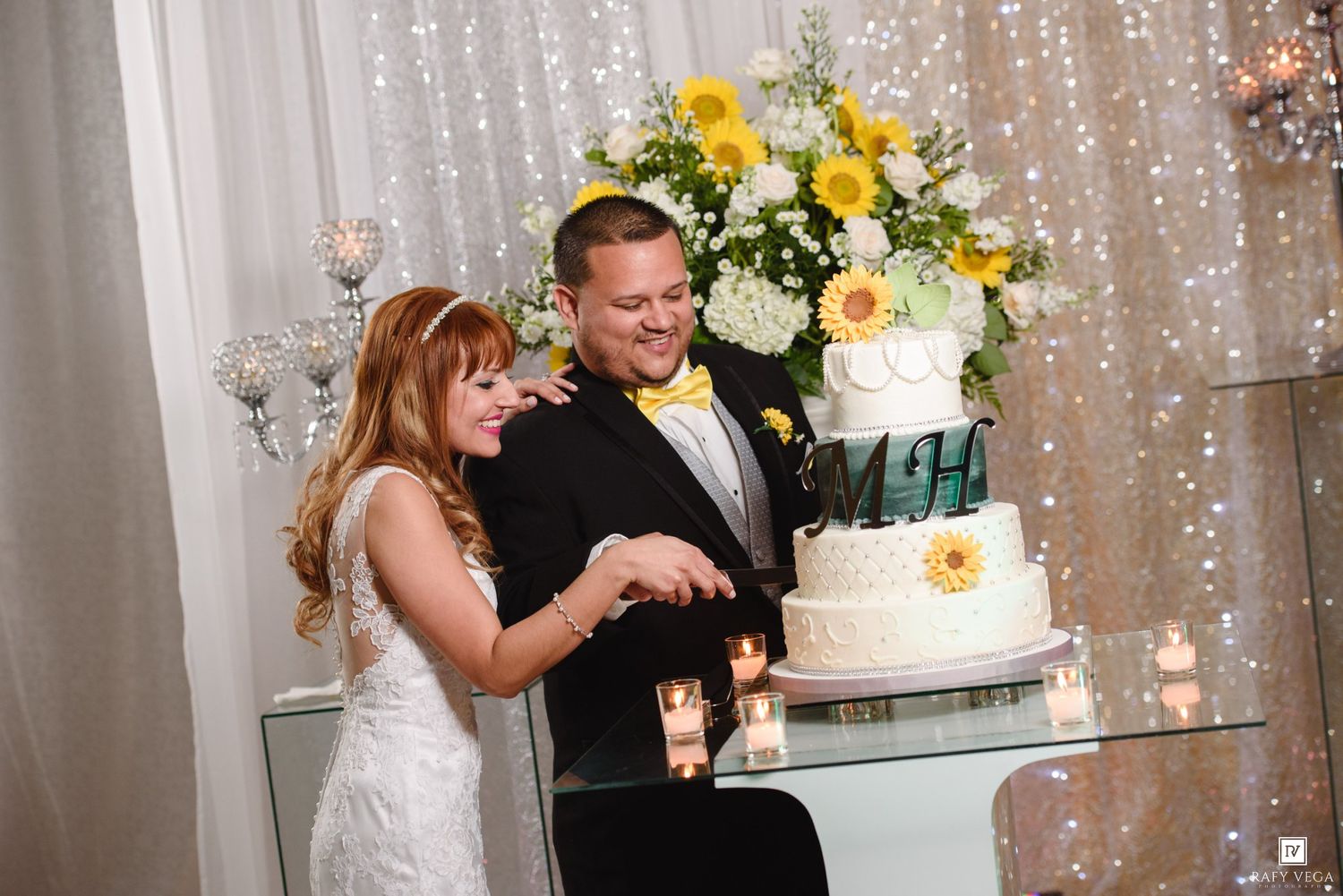 Bride and groom cutting their white wedding cake with yellow floral decor at elegant reception.