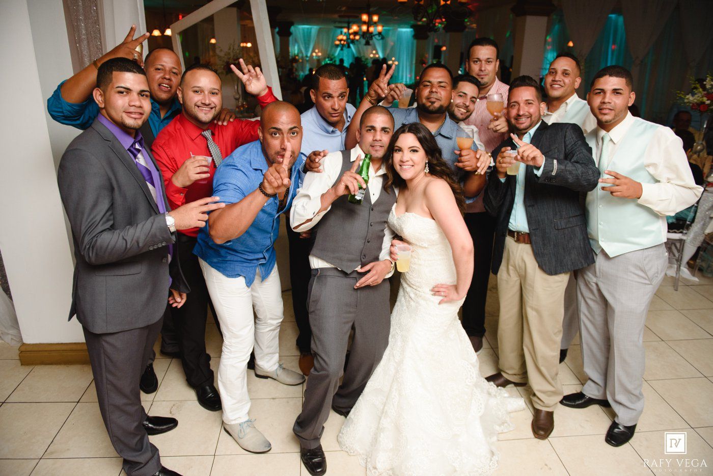 Bride and groom pose with groomsmen and guests at a festive wedding reception celebration.