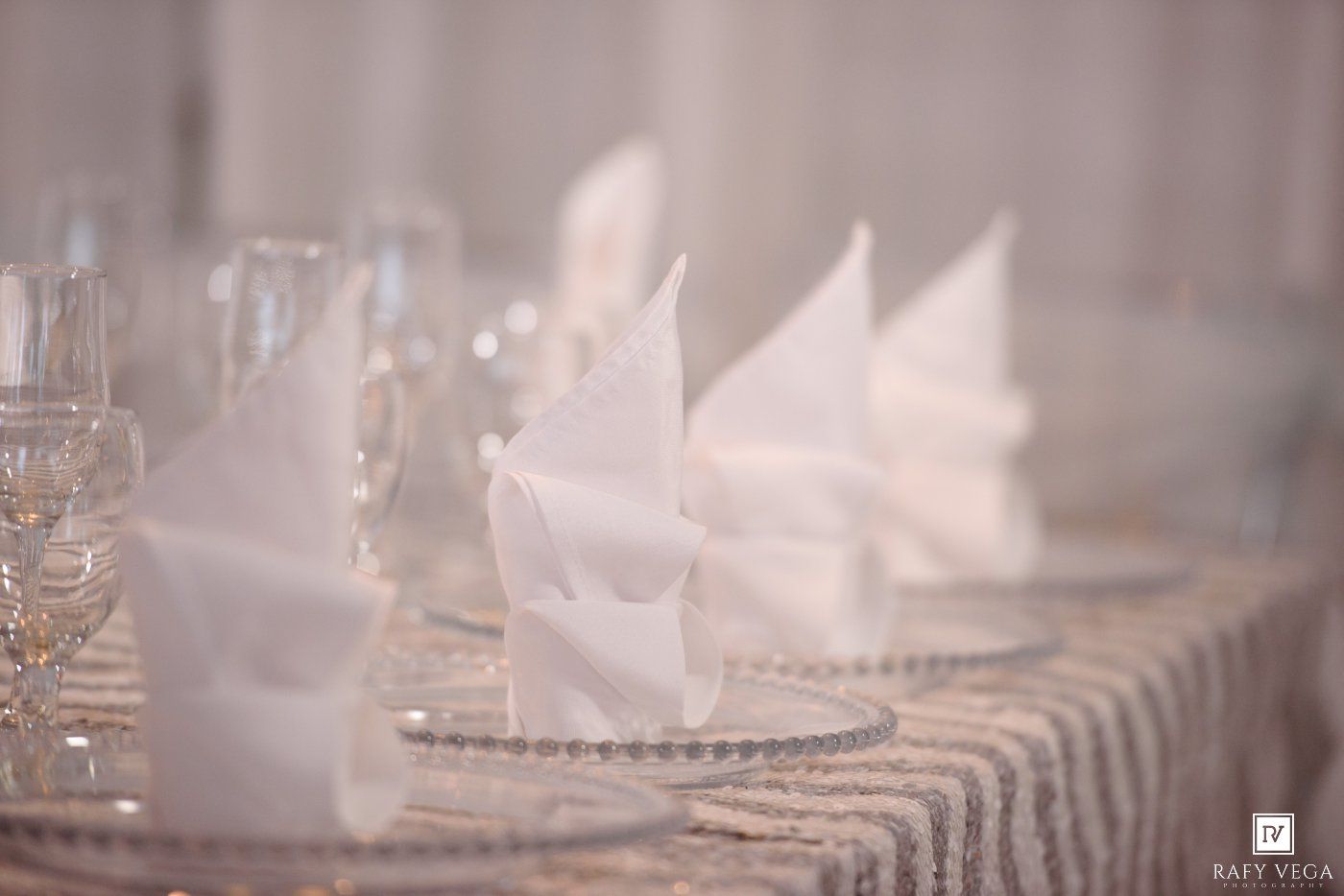 Elegant white folded napkins arranged on a striped tablecloth with crystal glassware at a formal wedding reception.