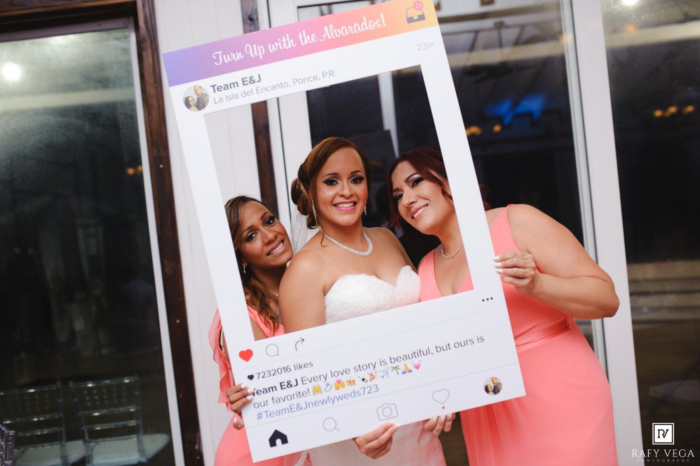 Three women pose together at a wedding reception holding a decorative Instagram-style photo frame prop.