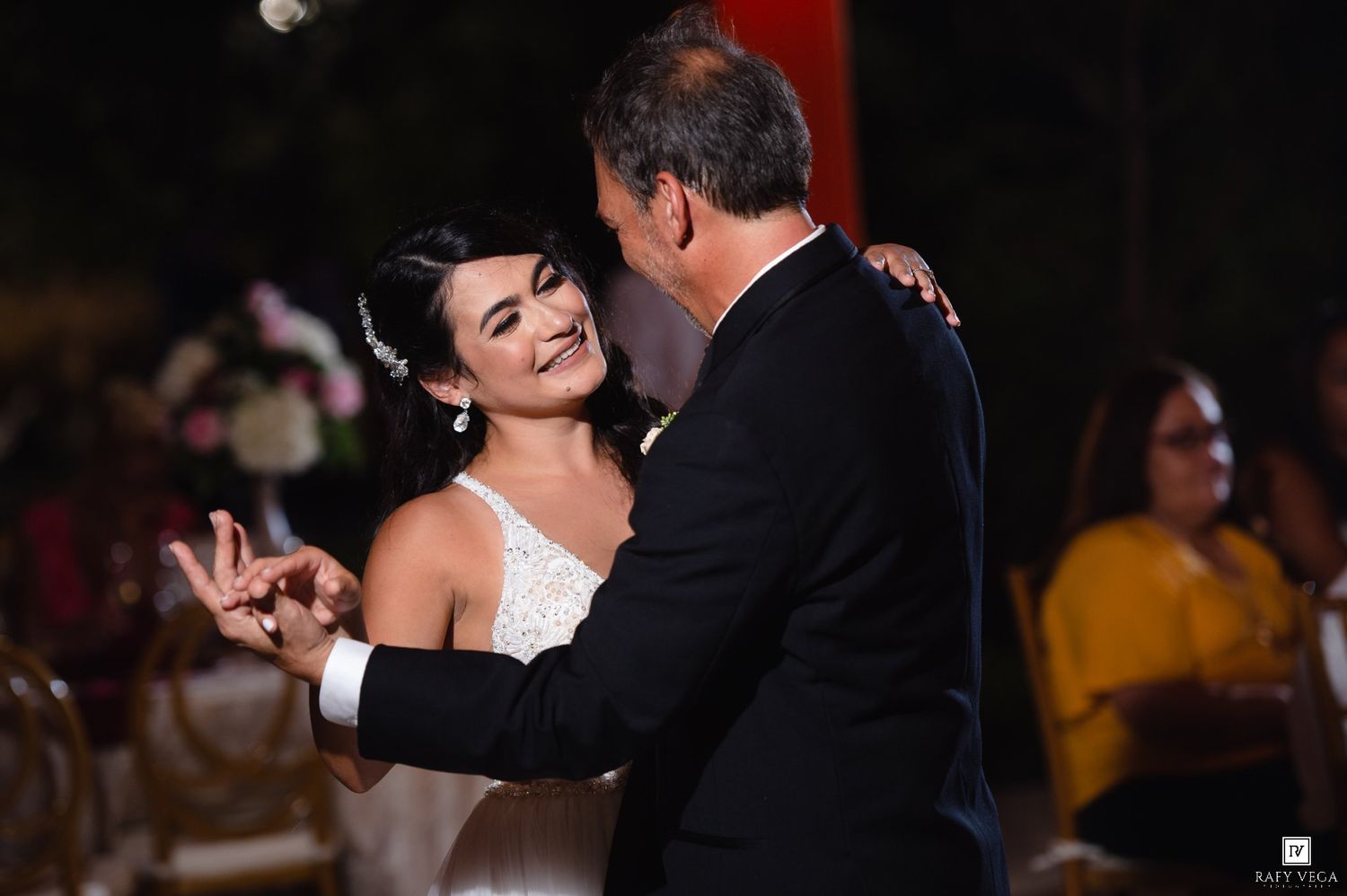 Bride in white gown shares a joyful first dance with a man in a black suit at an elegant wedding reception.