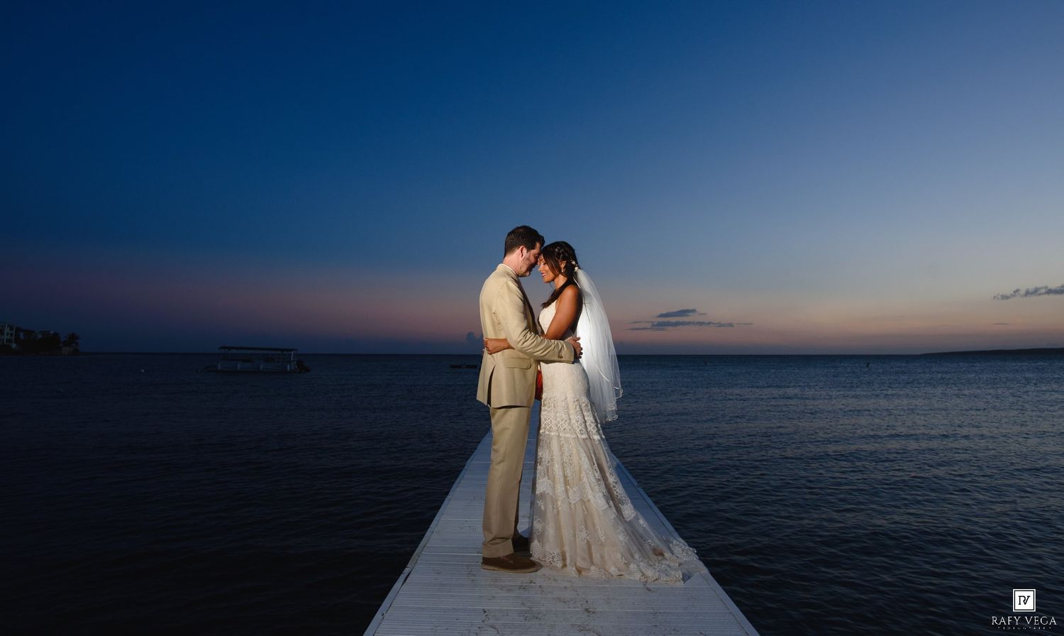 Bride and groom share romantic sunset moment on ocean pier, silhouetted against twilight sky in wedding attire.