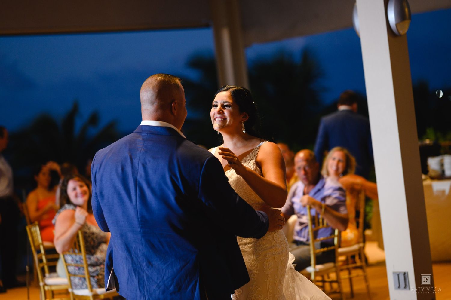 Bride and groom share their first dance at an outdoor evening wedding reception with guests watching.