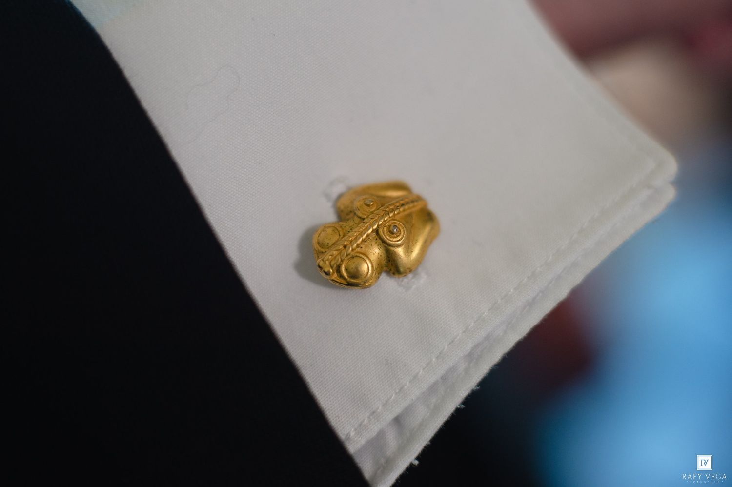 Close-up of a gold fleur-de-lis cufflink on a white dress shirt sleeve.