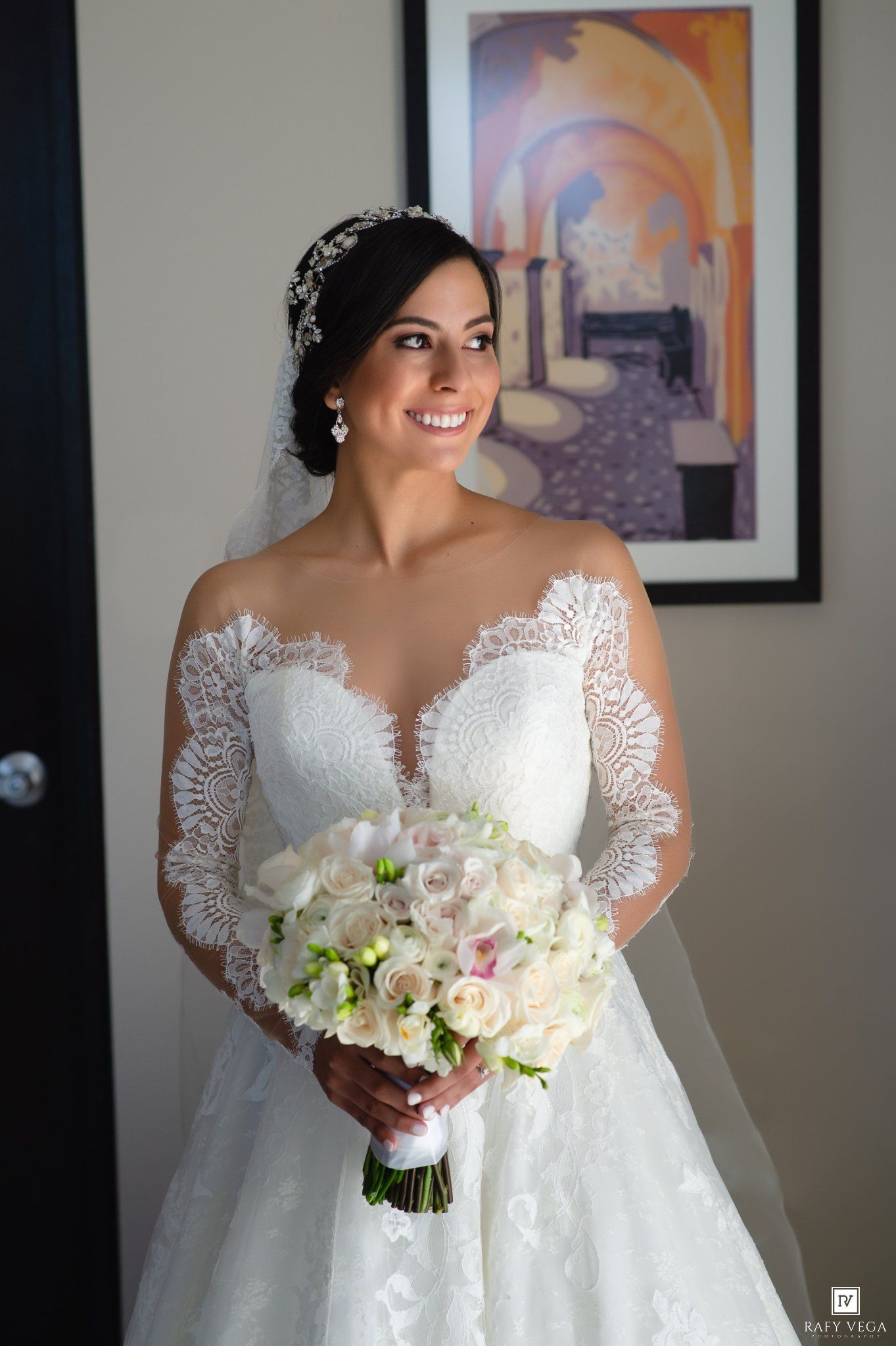 Elegant bride in long-sleeve lace wedding dress holding a white and pink floral bouquet.