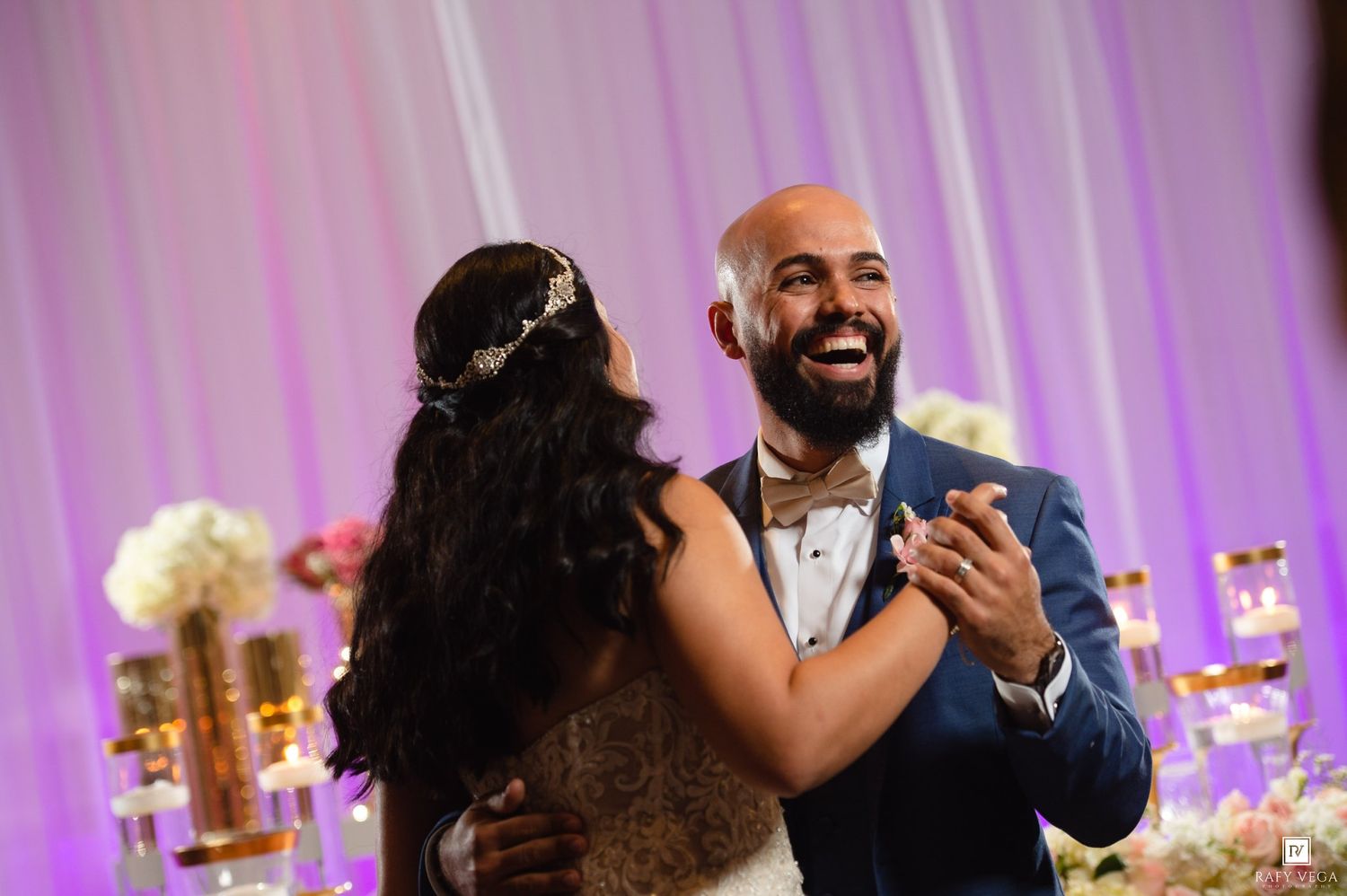 Bride and groom sharing their first dance, smiling joyfully at elegant floral wedding reception.