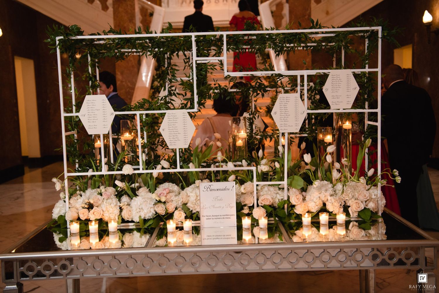 Elegant wedding display with white floral arrangements, candles, and greenery on a decorative metal frame stand.