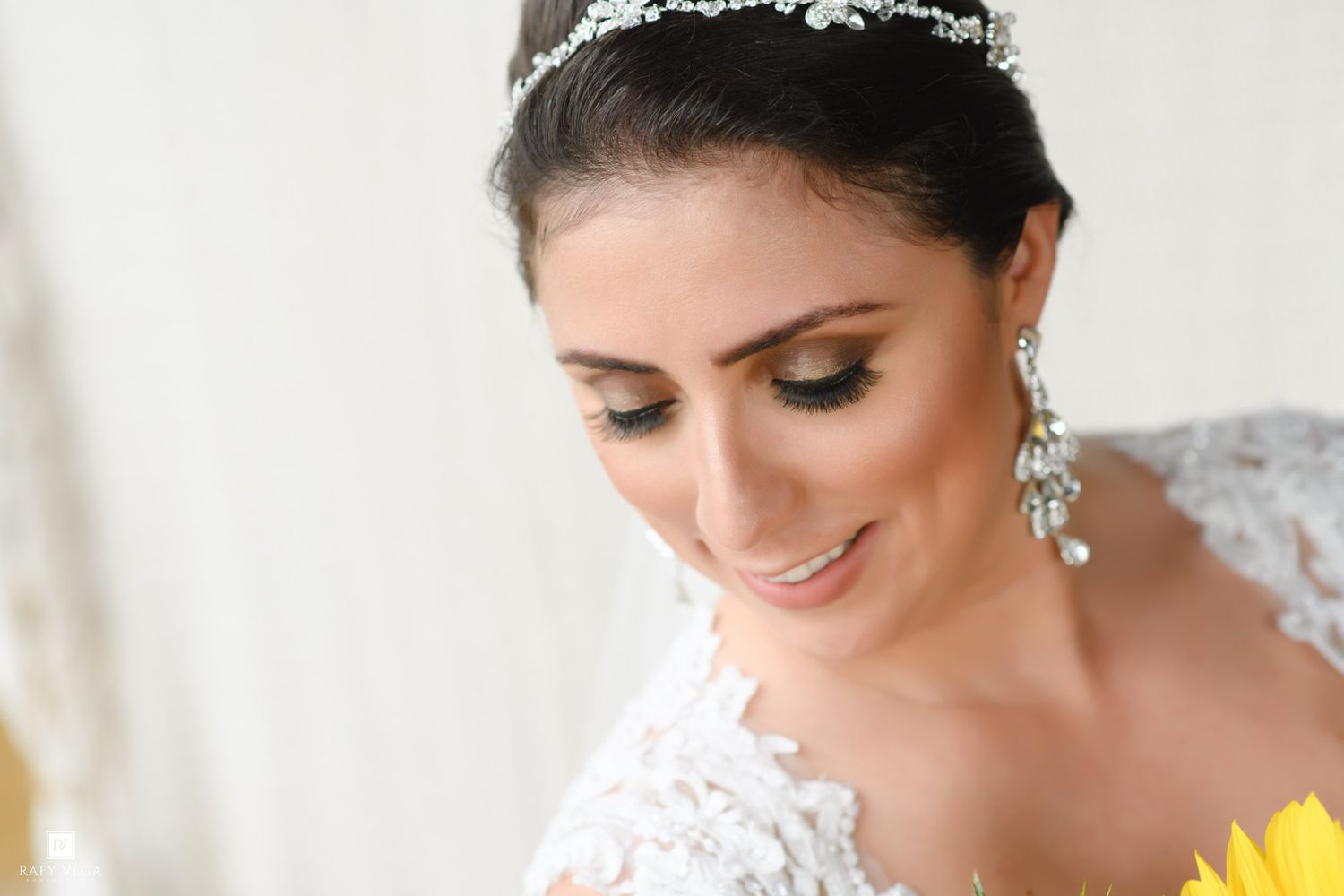Close-up of bride wearing lace gown, crystal tiara, and pearl drop earrings with elegant bridal makeup.