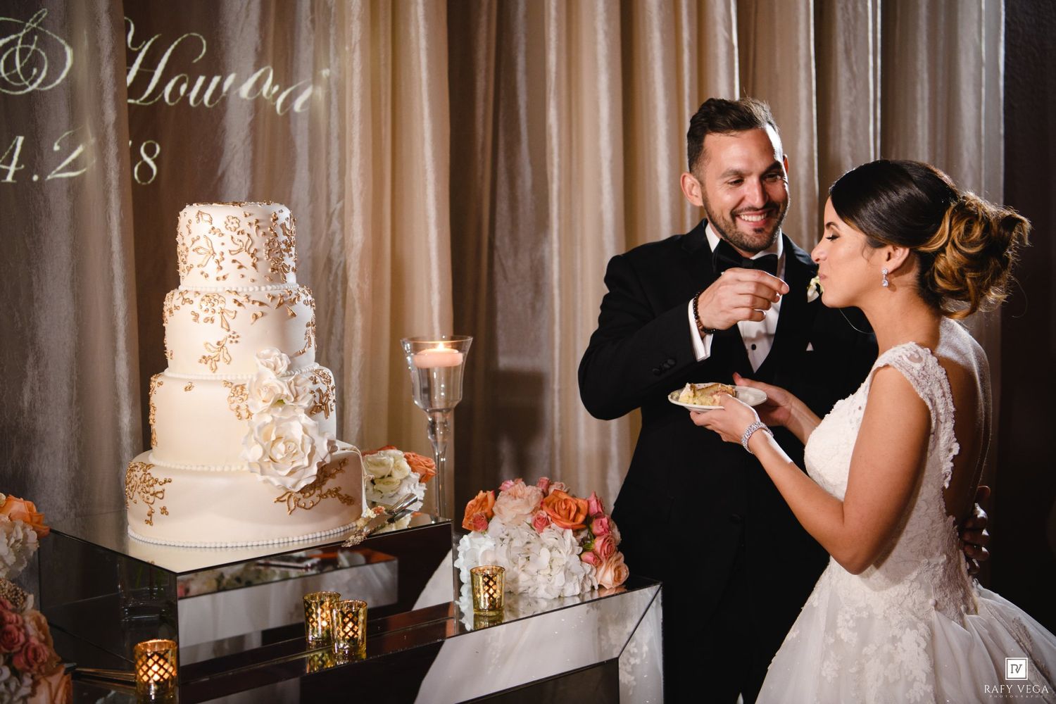 Bride and groom smiling while cutting their elegant four-tier white wedding cake at their reception.
