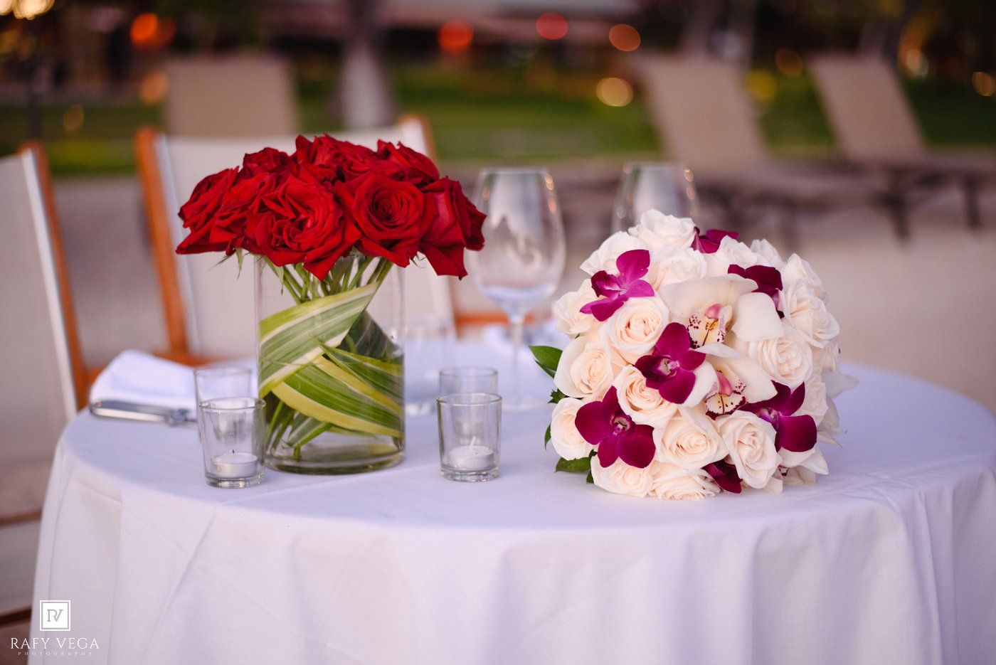Elegant wedding table with red rose centerpiece and white orchid bridal bouquet on white linen tablecloth.