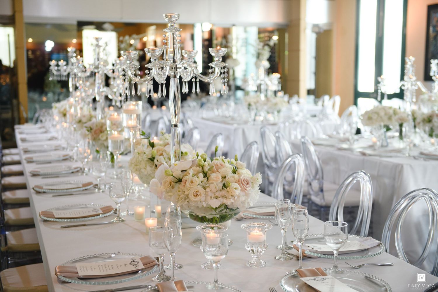 Luxurious wedding tablescape with crystal candelabras, white floral centerpieces, and glowing candles on white linens.
