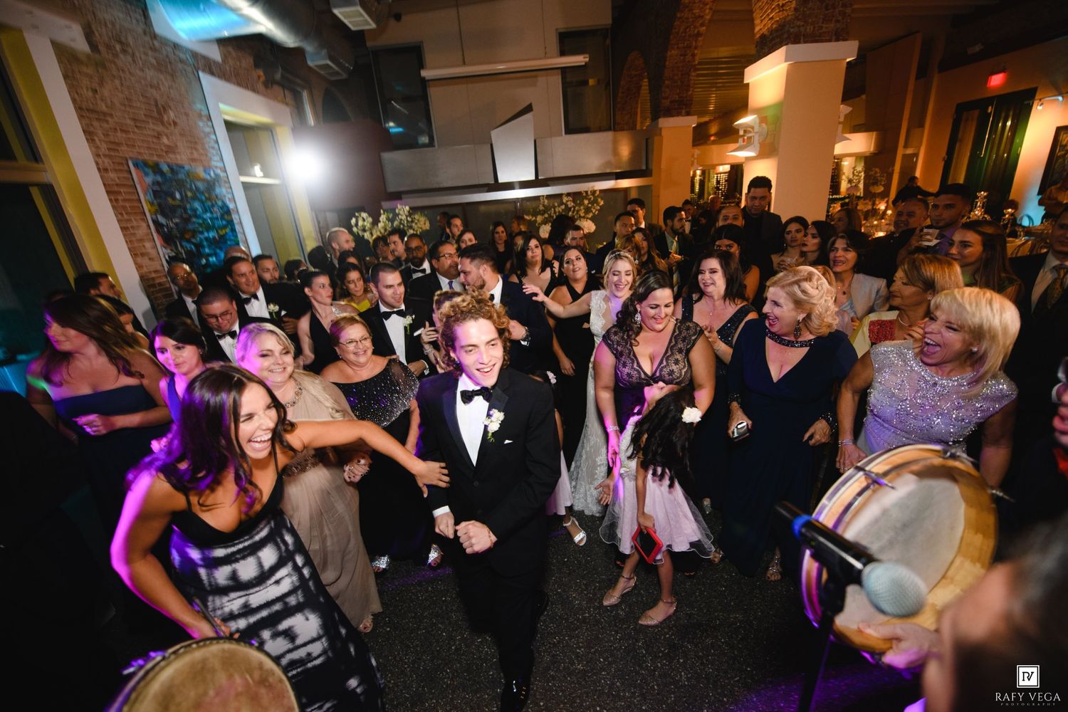 Elegant wedding reception with guests dancing in formal attire under warm lights.