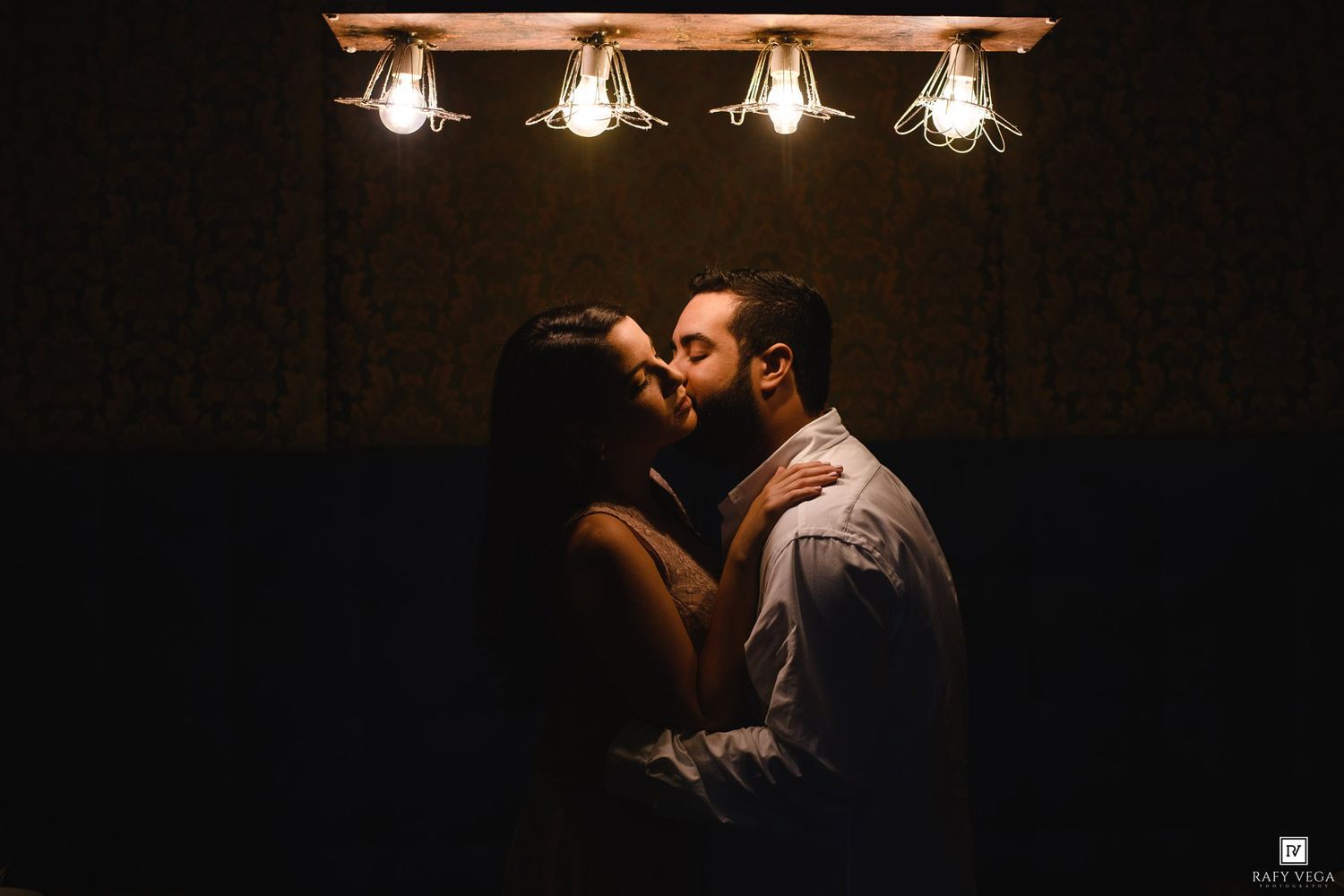 Romantic couple sharing an intimate moment under warm Edison bulb lights in a dimly lit room.