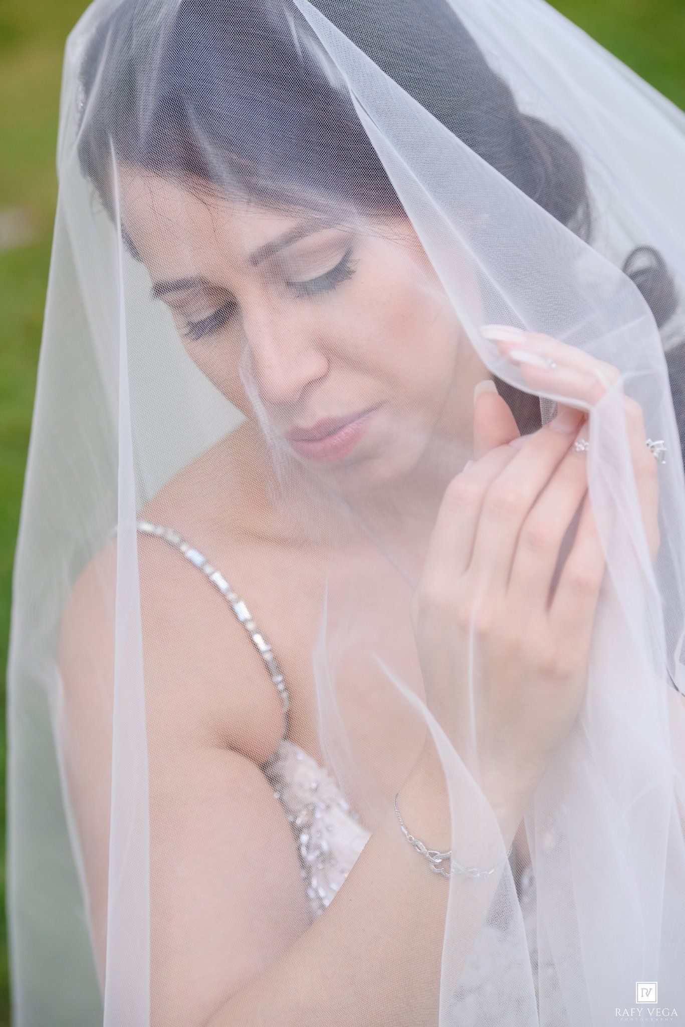 Bride in white lace gown and veil looking down, wearing silver necklace and bracelet in an elegant bridal portrait.
