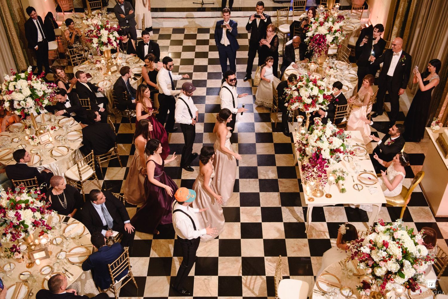 Aerial view of elegant wedding reception with black and white checkered dance floor, floral centerpieces, and guests mingling.