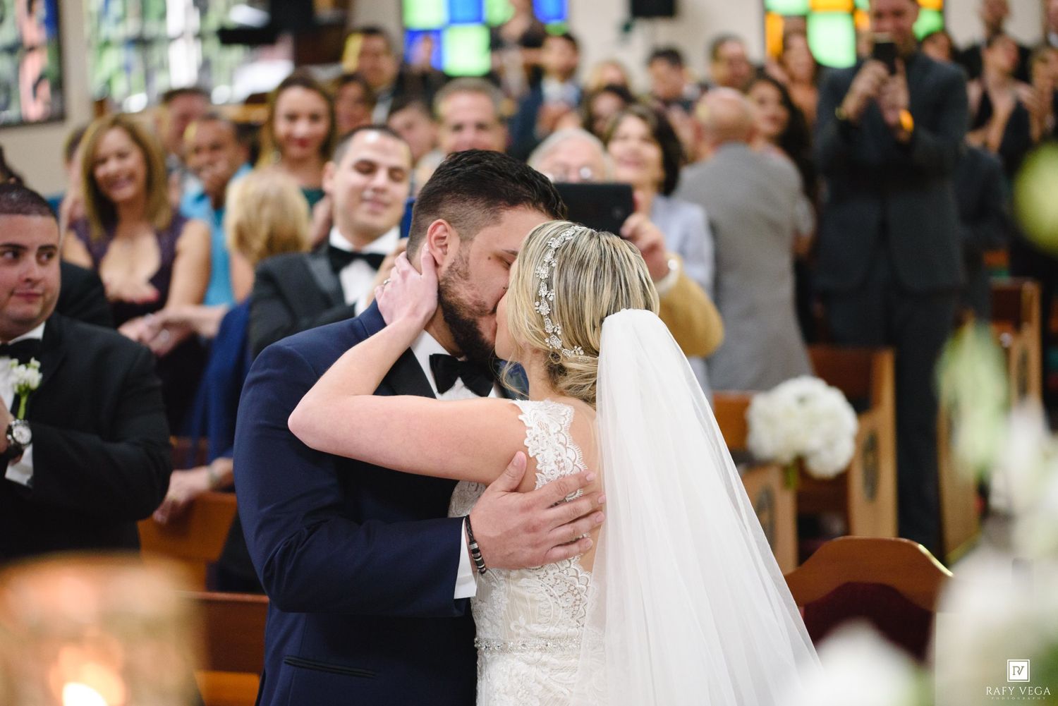 Bride and groom share their first kiss at the altar during a church wedding ceremony with guests watching.