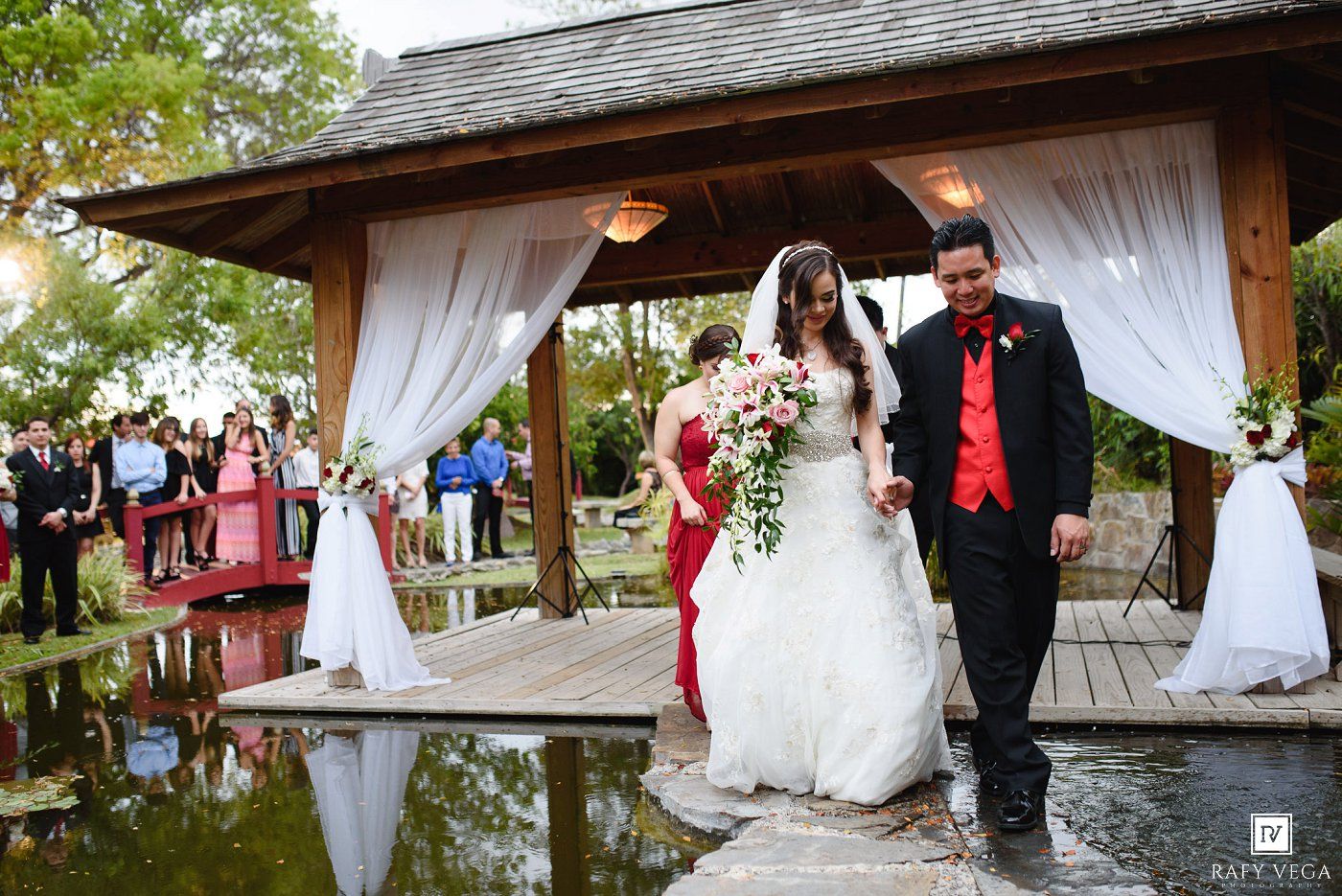 Bride and groom walk hand-in-hand down the aisle at an outdoor wedding ceremony by a pond.