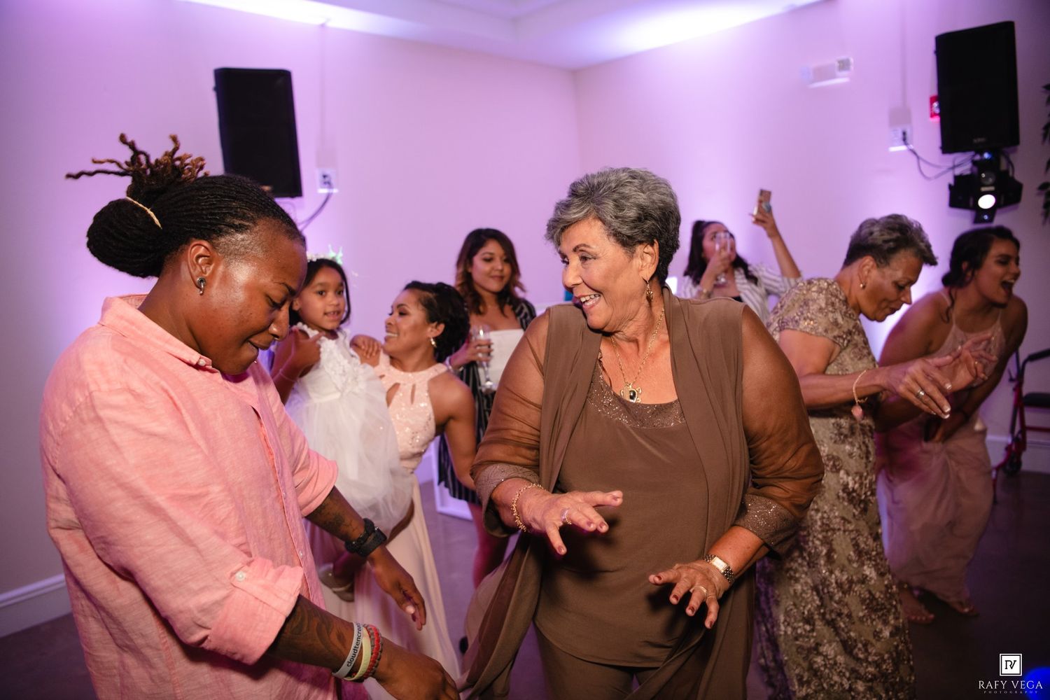 Two women dancing joyfully at an elegant wedding reception with guests celebrating in the background.