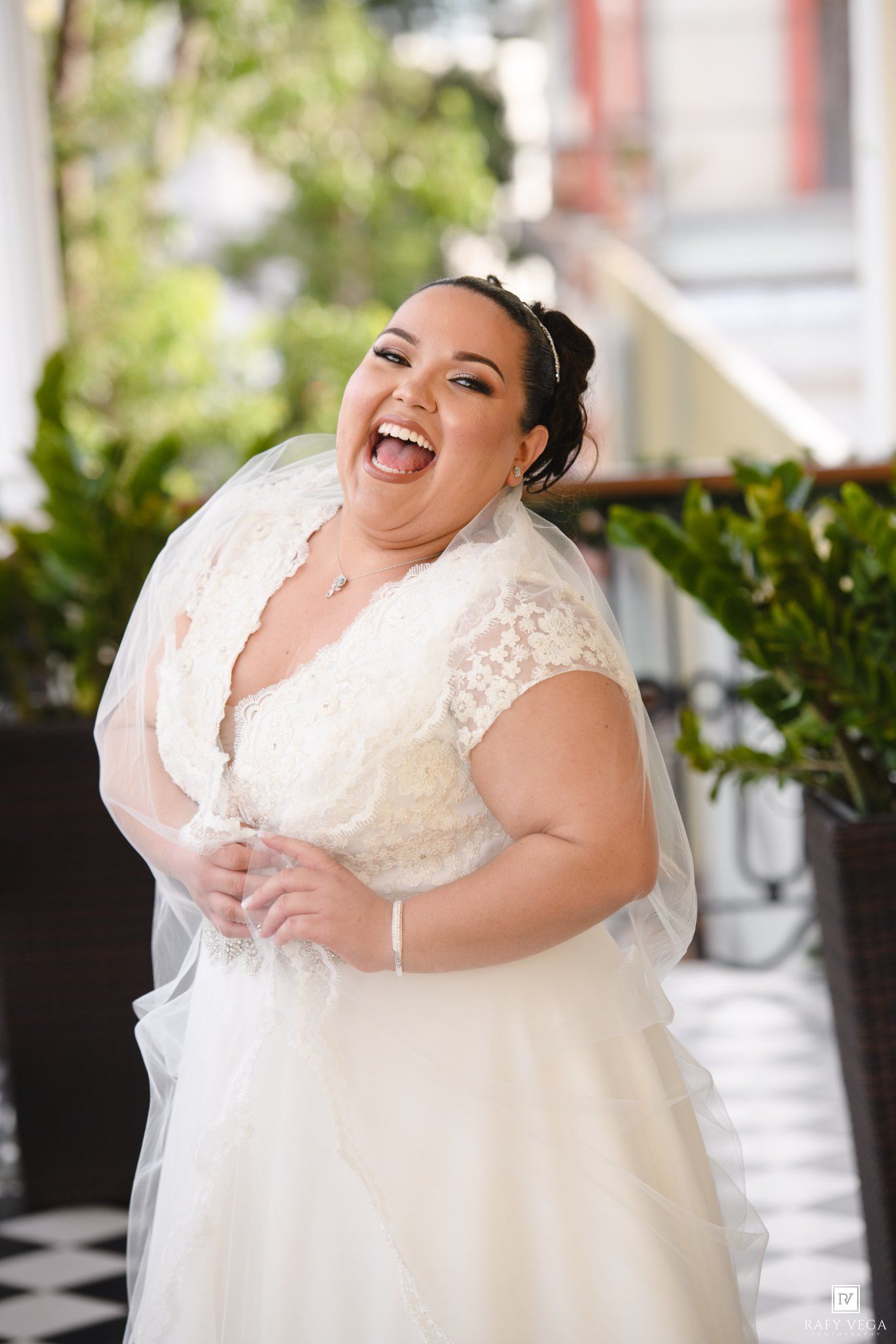 Joyful bride in white lace wedding dress laughing on outdoor balcony.