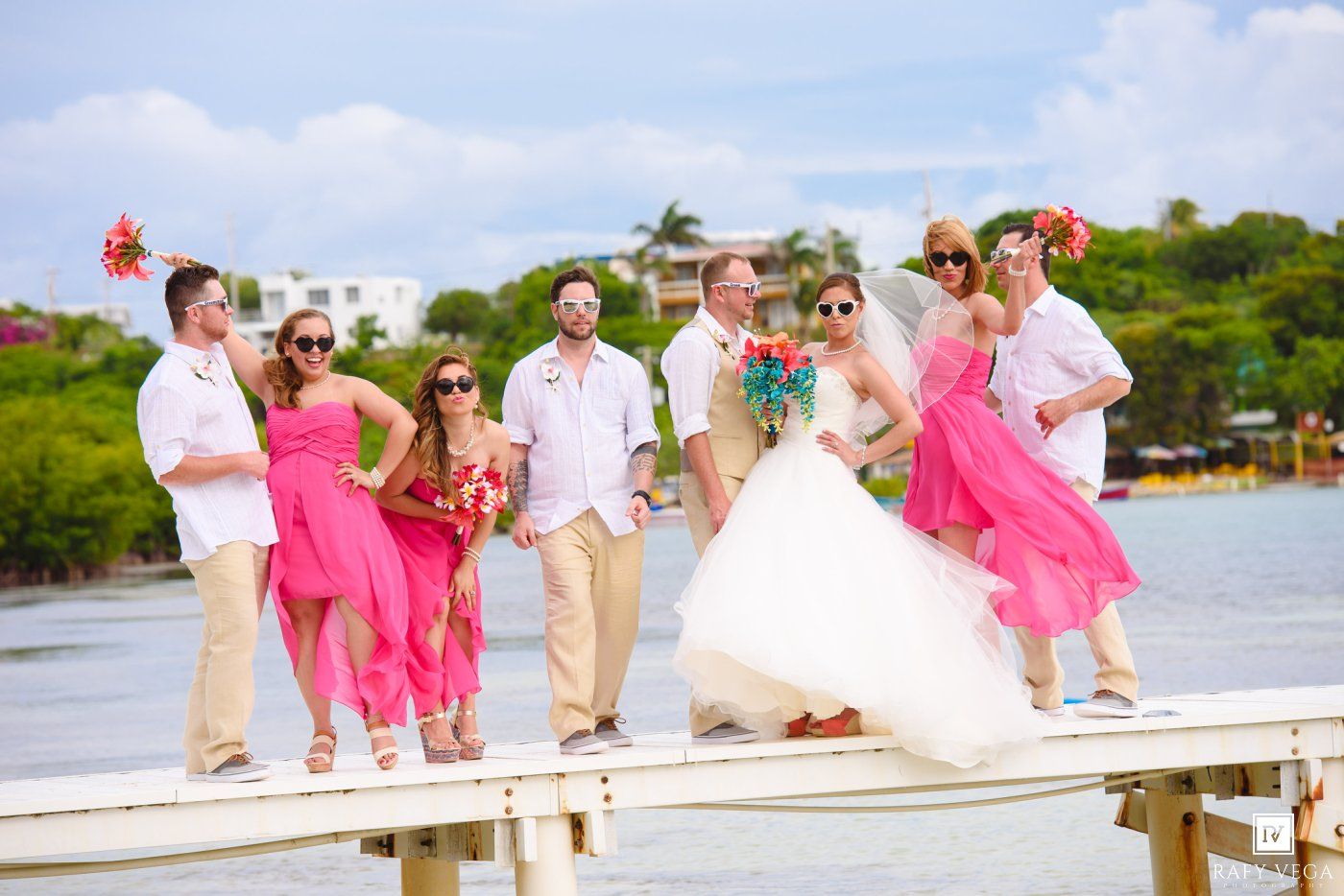 Wedding party posing on a dock in tropical destination, bridesmaids in pink dresses with bride and groomsmen in khaki.