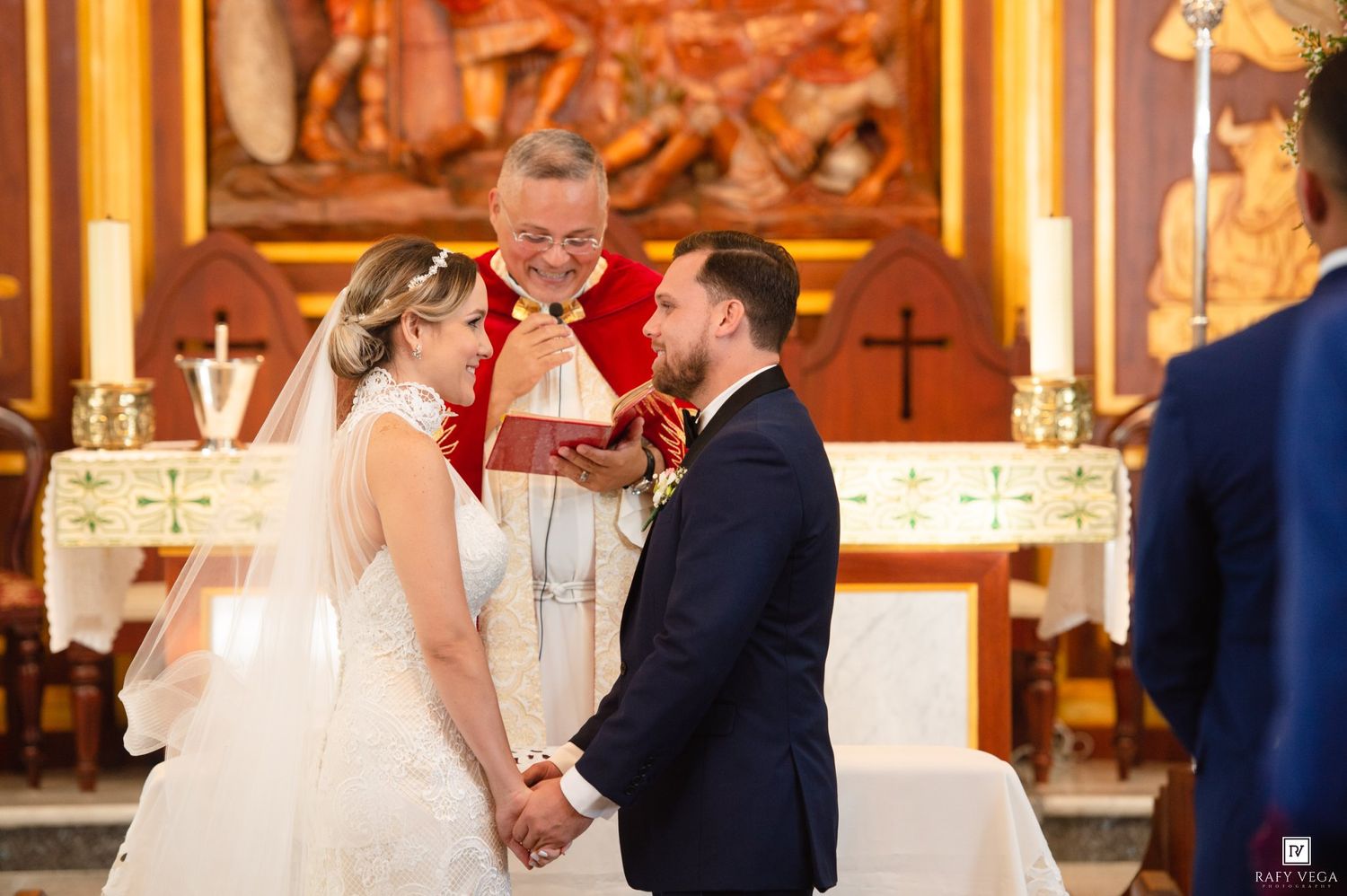 Bride and groom exchange vows at church altar with officiant in red vestments during elegant wedding ceremony.