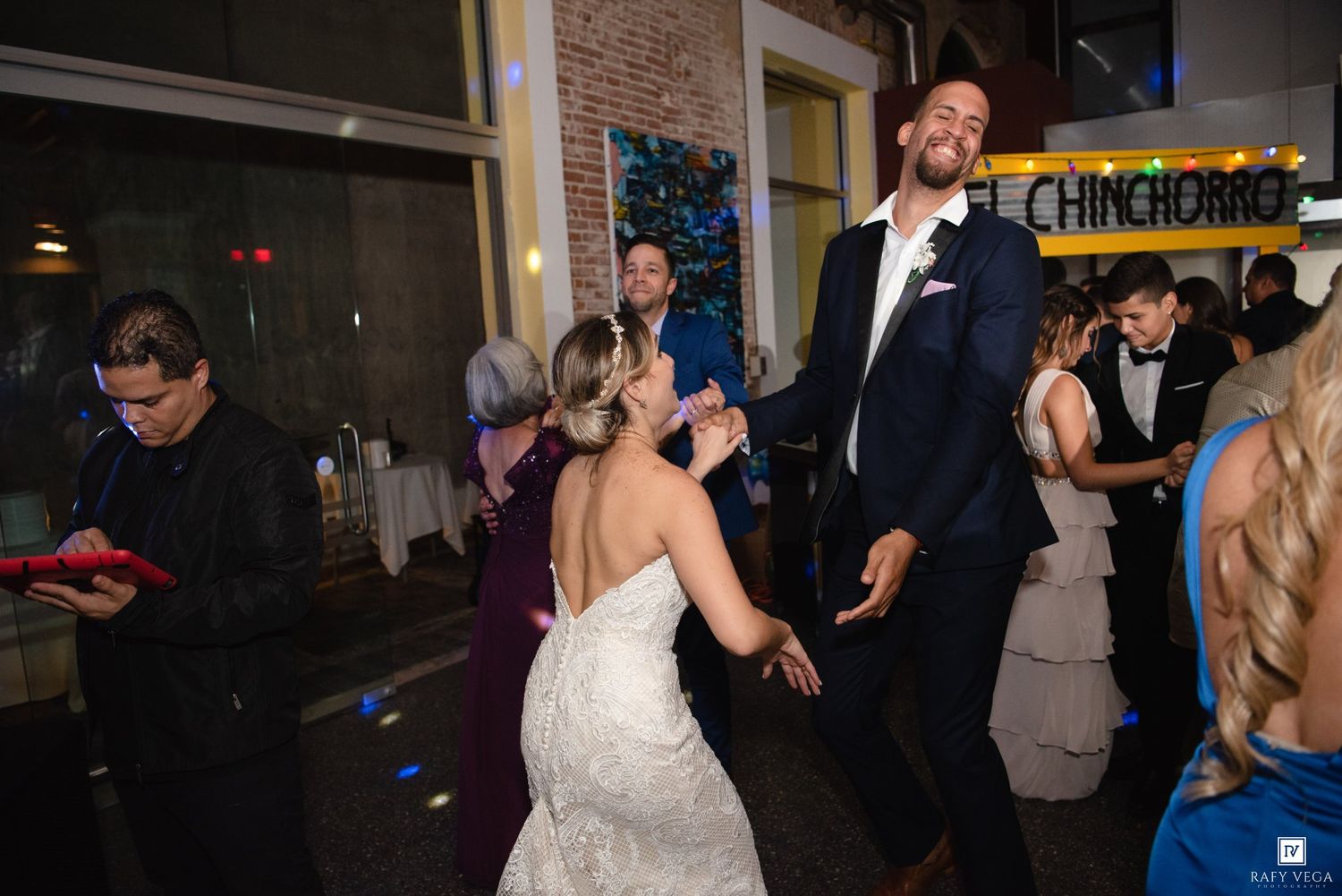 Bride and groom dancing joyfully at wedding reception with guests celebrating in background at elegant venue.
