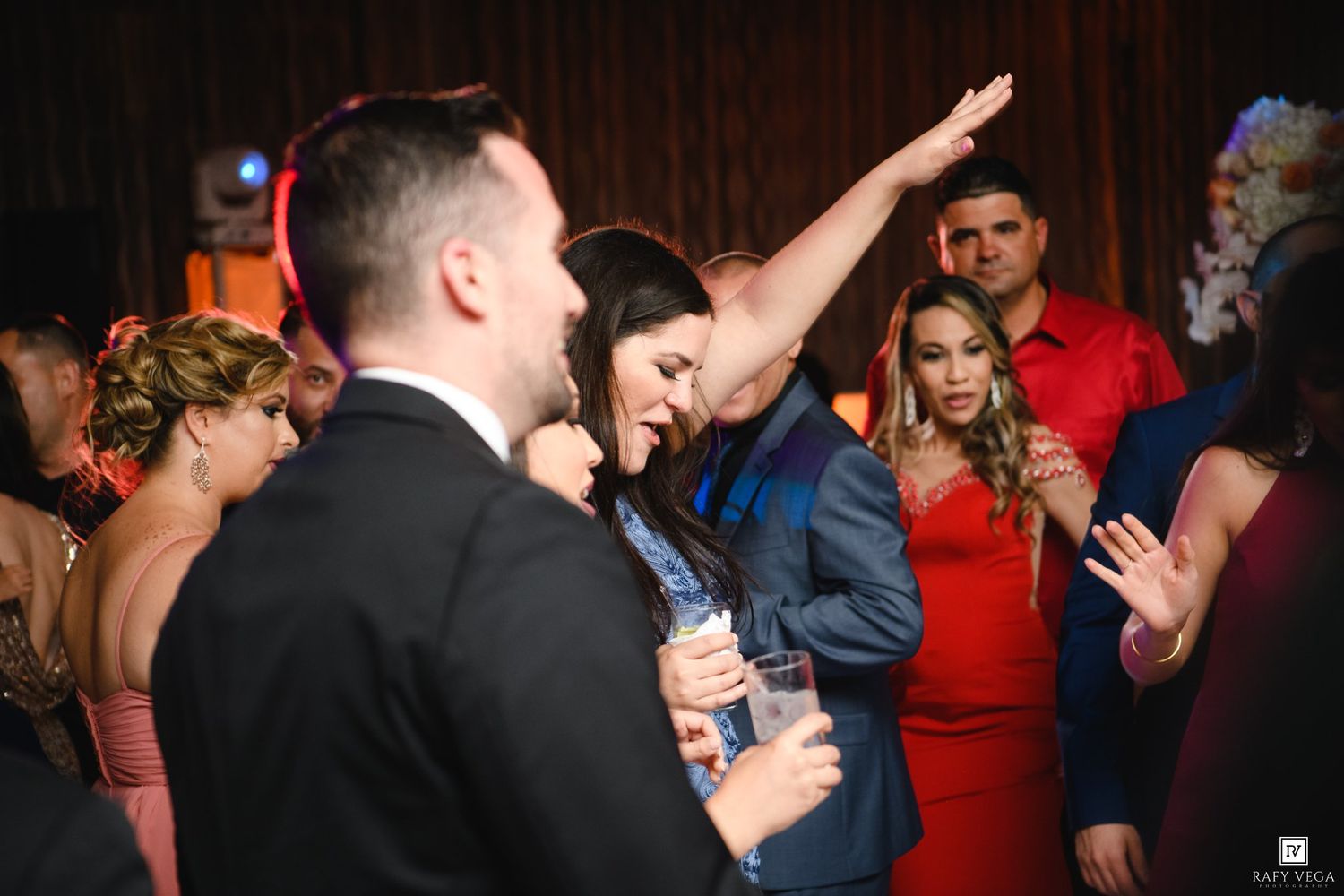 Guests dancing and celebrating at an elegant indoor party, woman in blue suit raises arm joyfully.