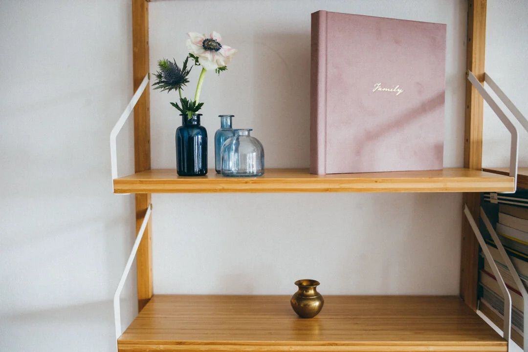 Wooden shelf with blue glass vases holding white flowers, a pink journal, and a small brass vase.
