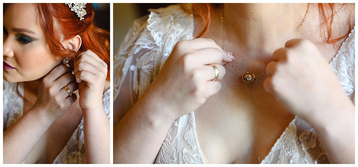 Red-haired bride putting on earrings and fastening a necklace while getting ready in a white lace wedding dress.