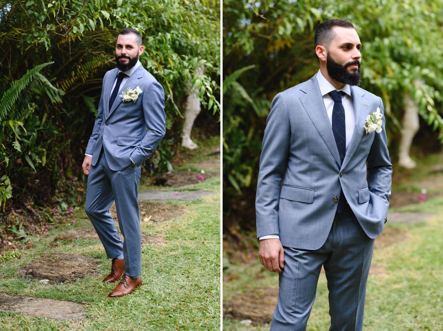 Groom in a light gray suit with navy tie and boutonniere poses outdoors among lush greenery for wedding photos.